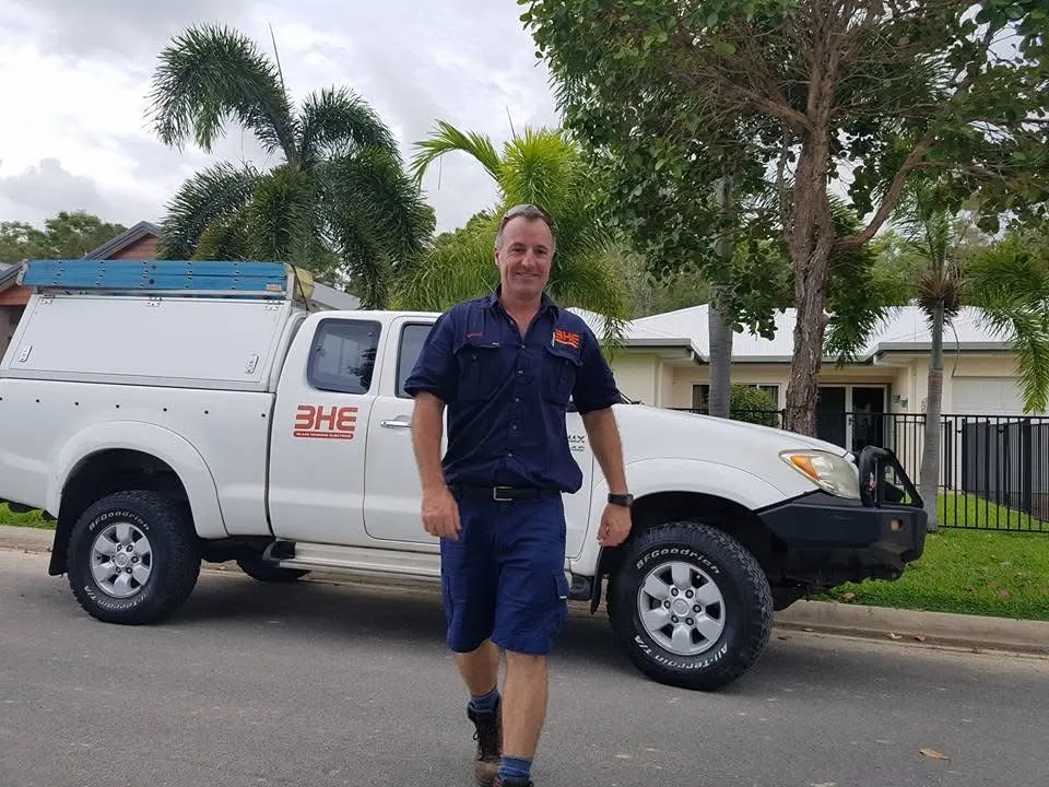 Brad Sims in work uniform walking past his ute on a suburban street, both carrying the early orange 3HE Blake Henning Electrics livery