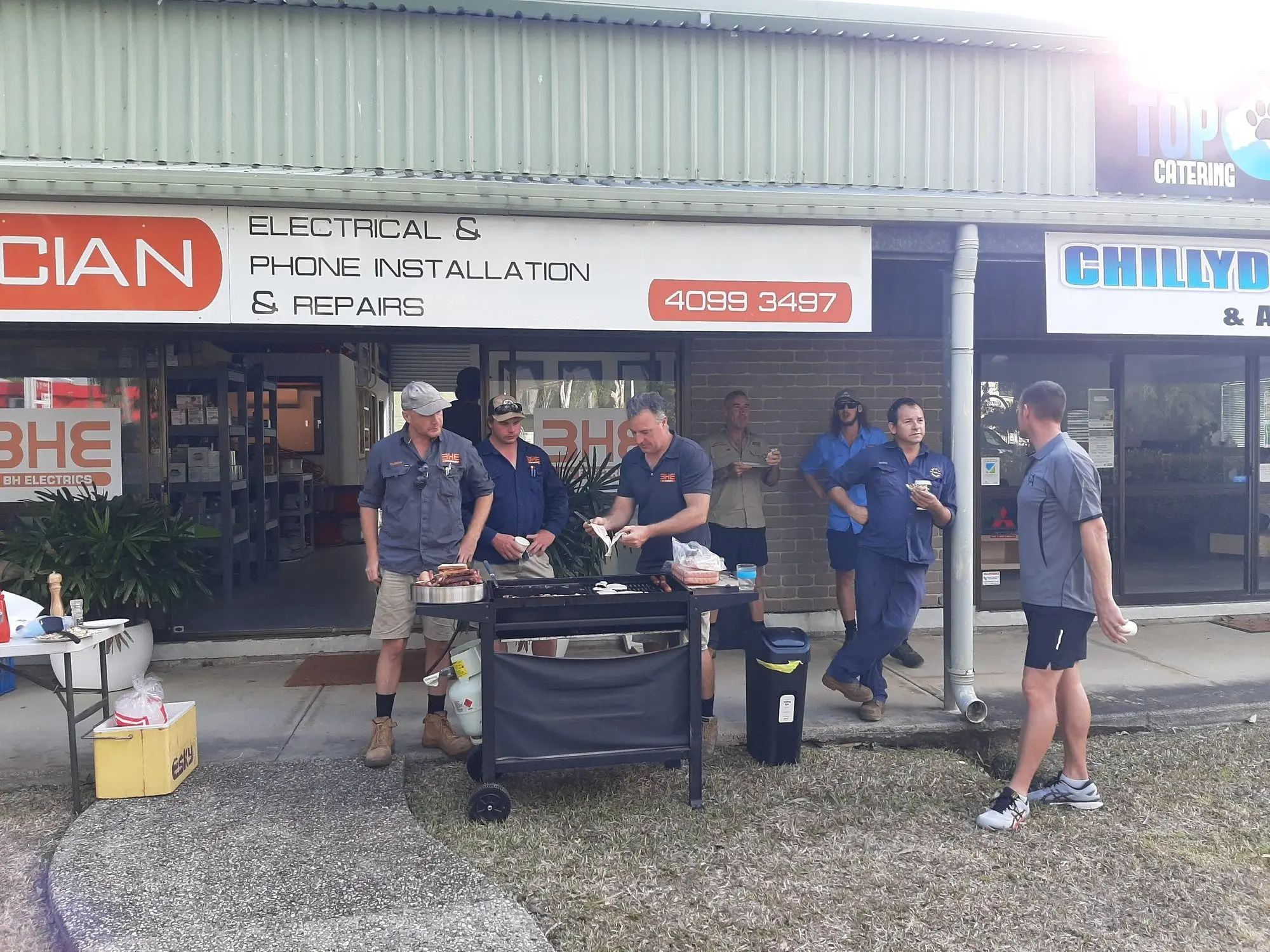 The BH Electrics crew at a barbecue outside the Craiglie workshop, snags on the grill and everyone standing about with a plate