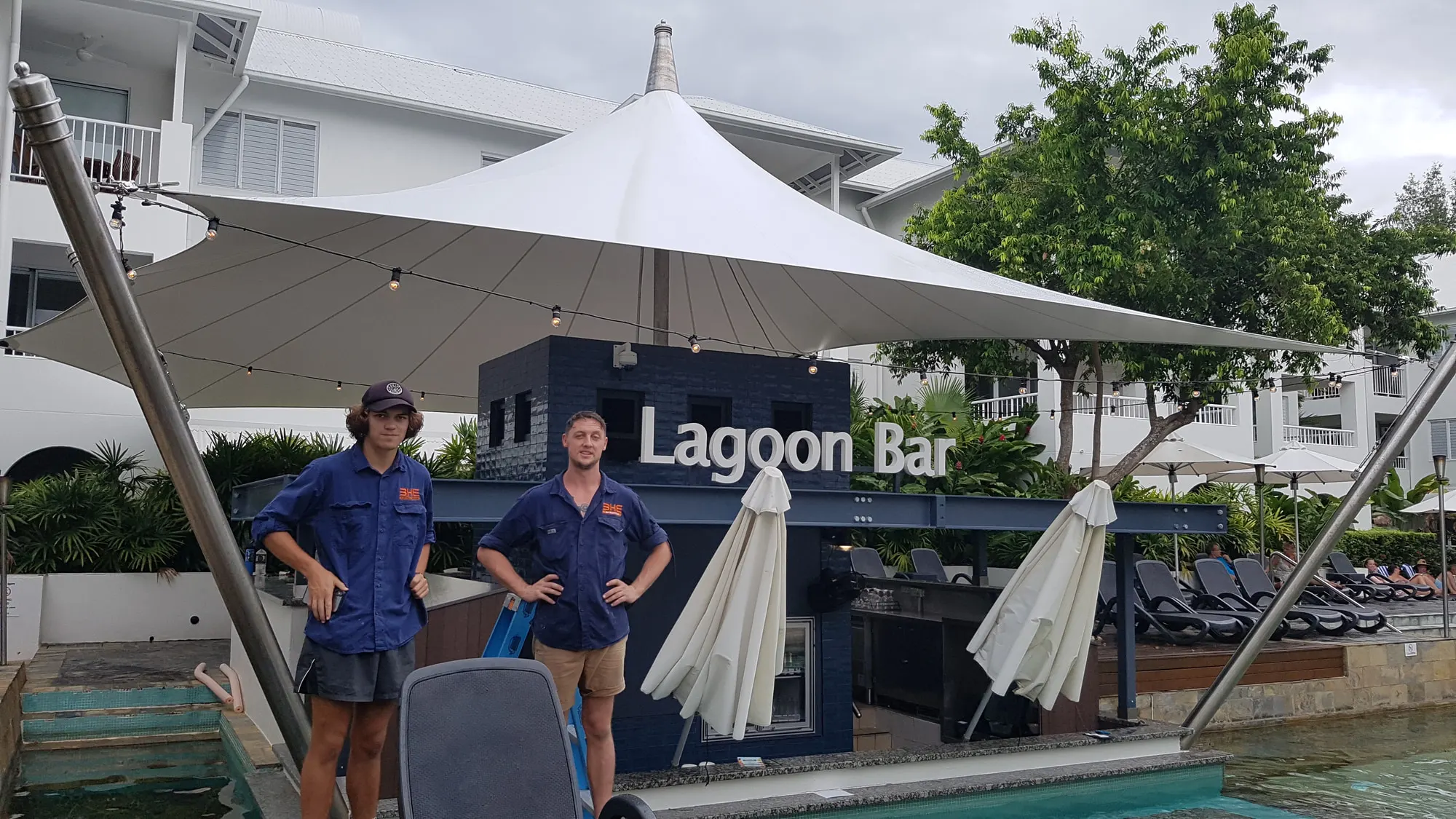 Two BH Electrics electricians in uniform beside the Lagoon Bar at a Port Douglas resort pool