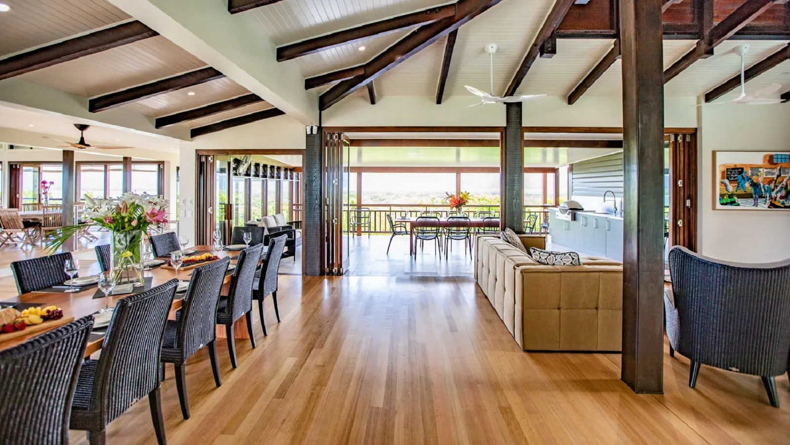 Open plan living and dining at Bangalow, Port Douglas, ceiling fans and downlights in a raked timber ceiling, bifolds open to the deck
