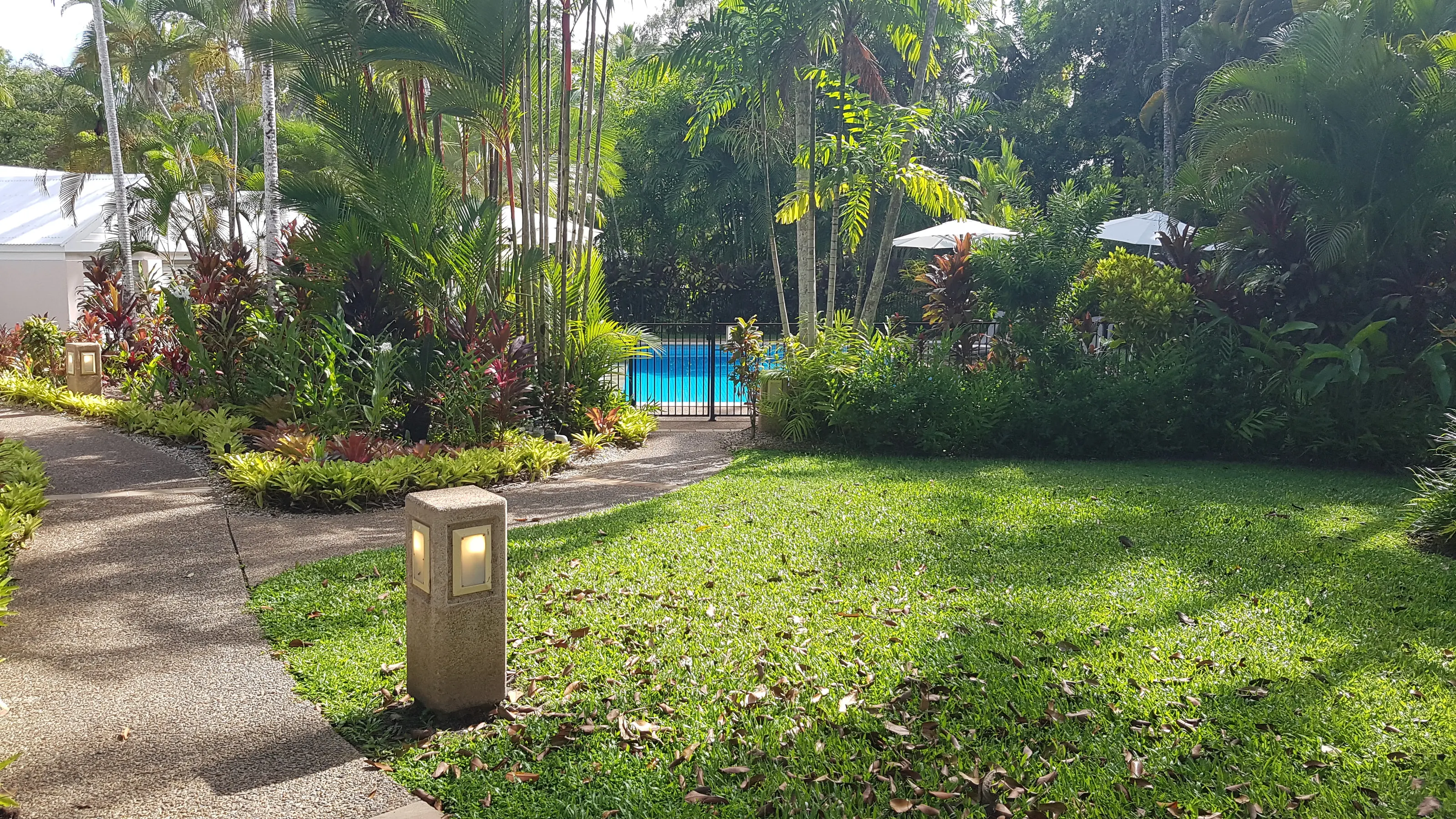 A garden bollard light on a resort lawn, palms and the pool behind it