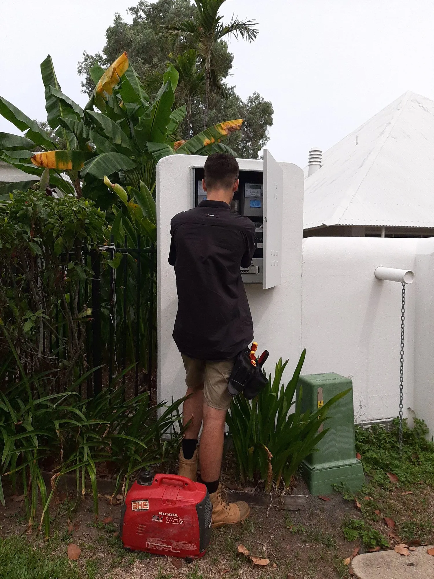 A BH Electrics electrician working inside an outdoor meter box, with a portable Honda inverter generator on the ground beside him