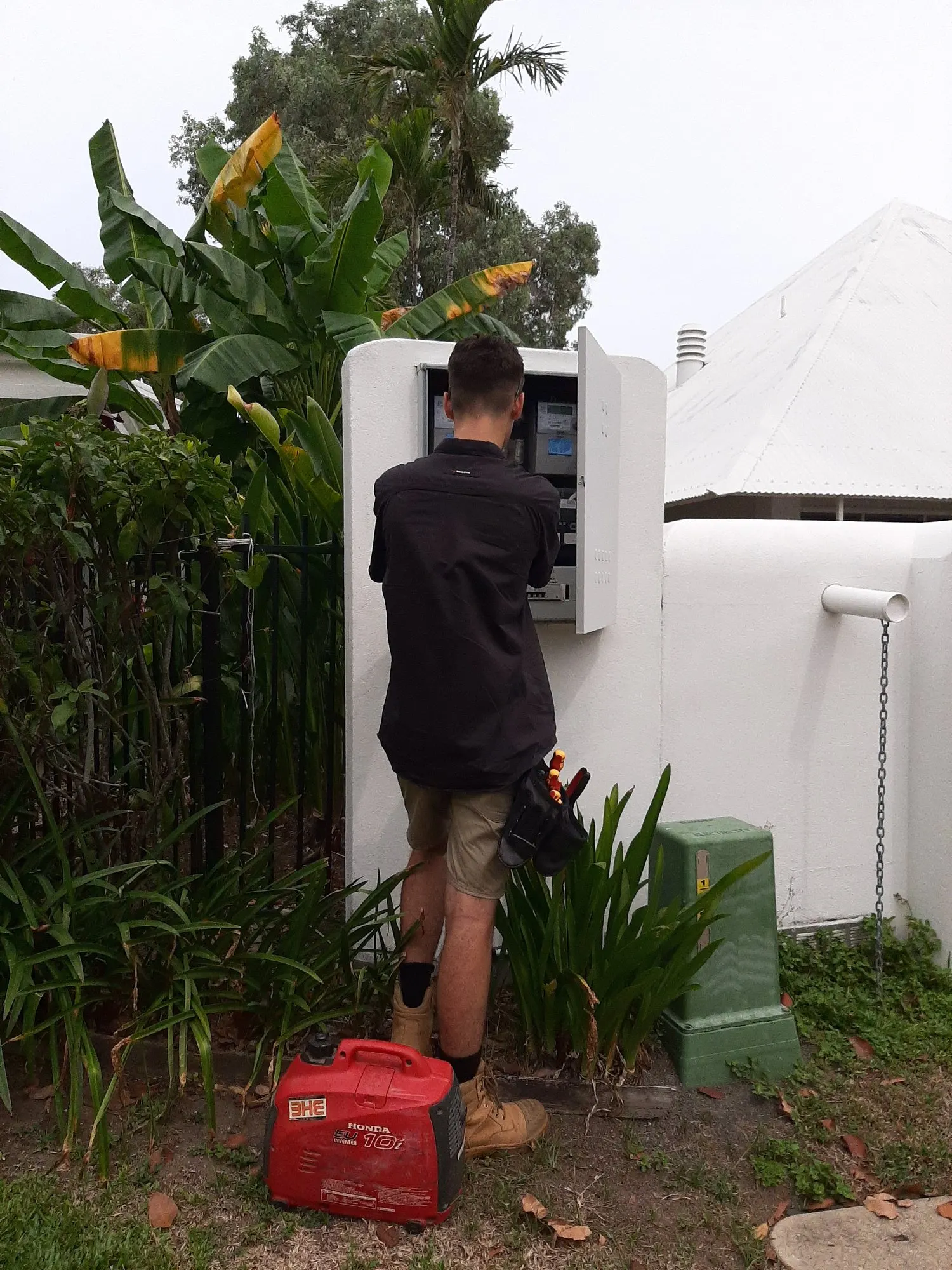 A BH Electrics electrician working inside an outdoor meter box, with a portable Honda inverter generator on the ground beside him