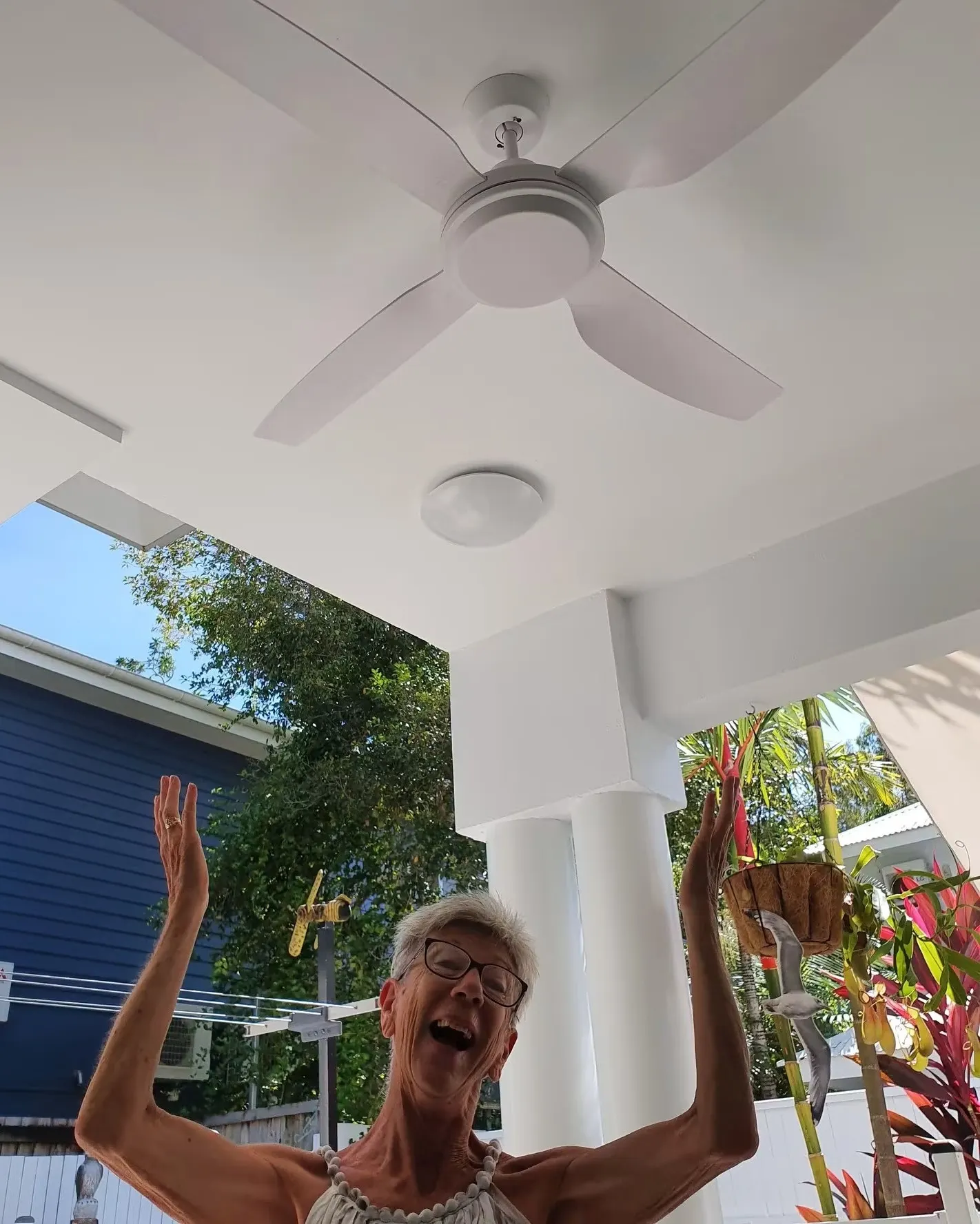 A customer standing under her newly installed ceiling fan on a covered patio, both arms in the air, laughing