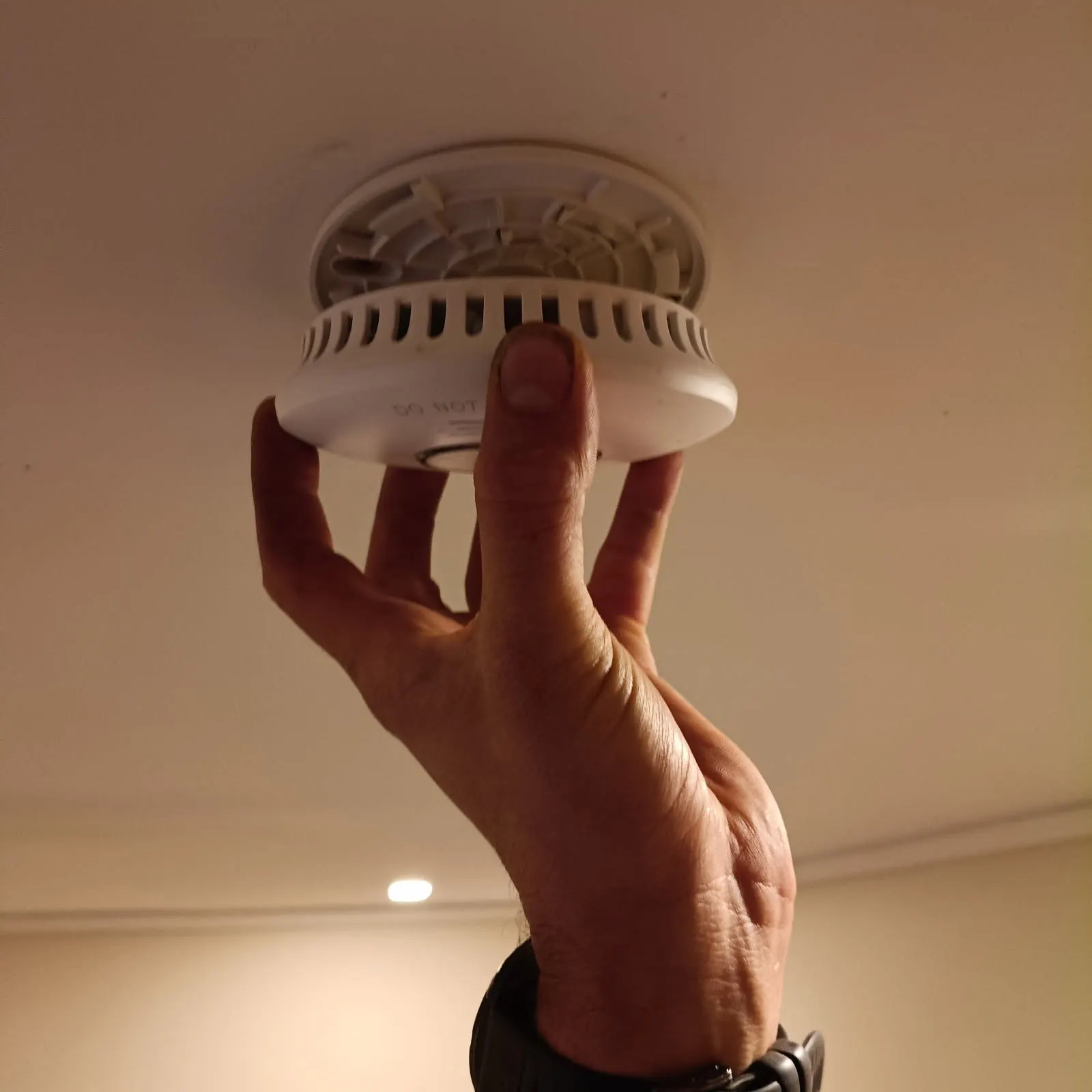 Pressing the test button on a ceiling mounted smoke alarm