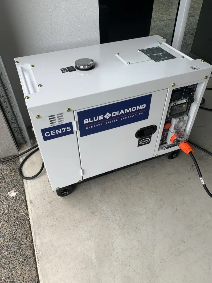 A silenced diesel generator on a concrete slab with the changeover lead plugged in
