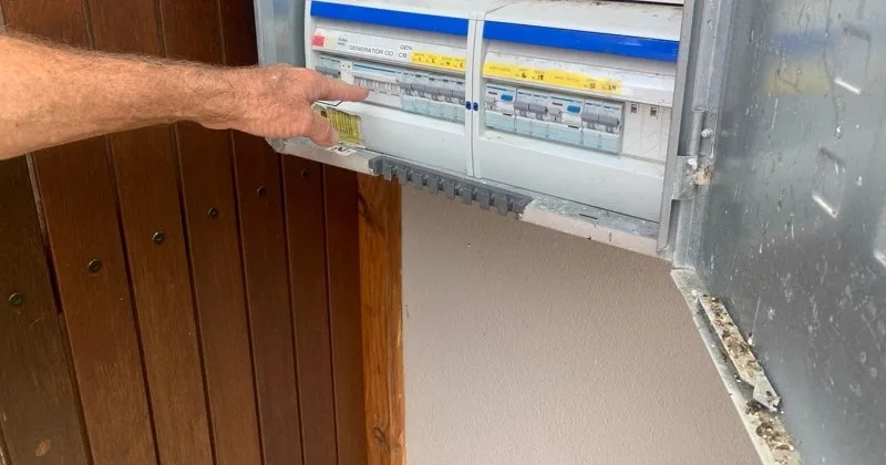 A hand on the generator changeover breaker in a switchboard, labelled and grouped with the circuit breakers it feeds