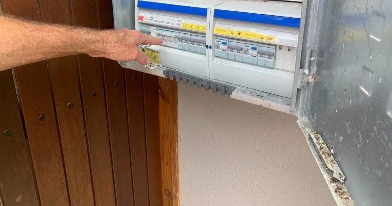 A hand on the generator changeover breaker in a switchboard, labelled and grouped with the circuit breakers it feeds