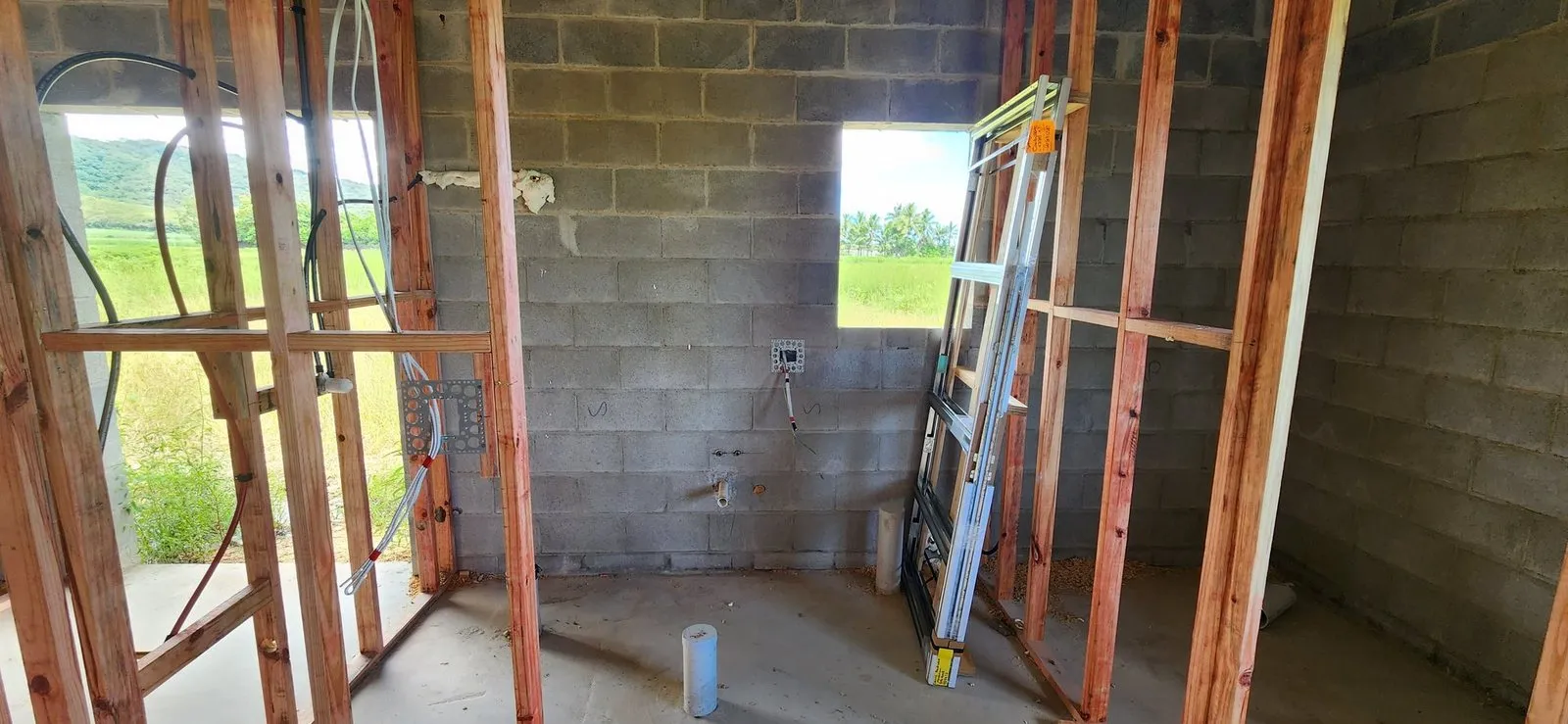 Rough-in cabling run through timber framing against blockwork on a new house, cane fields beyond