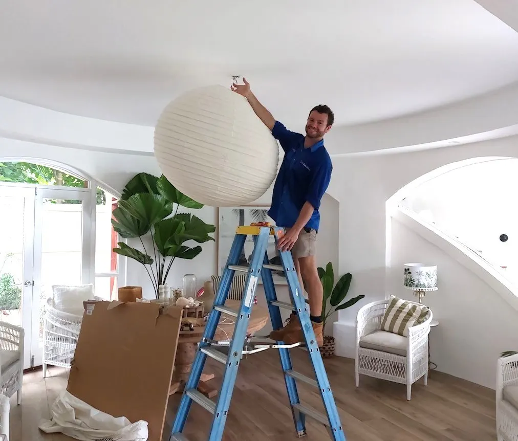 A BH Electrics electrician on a step ladder fitting a large paper pendant light in a renovated Port Douglas living room