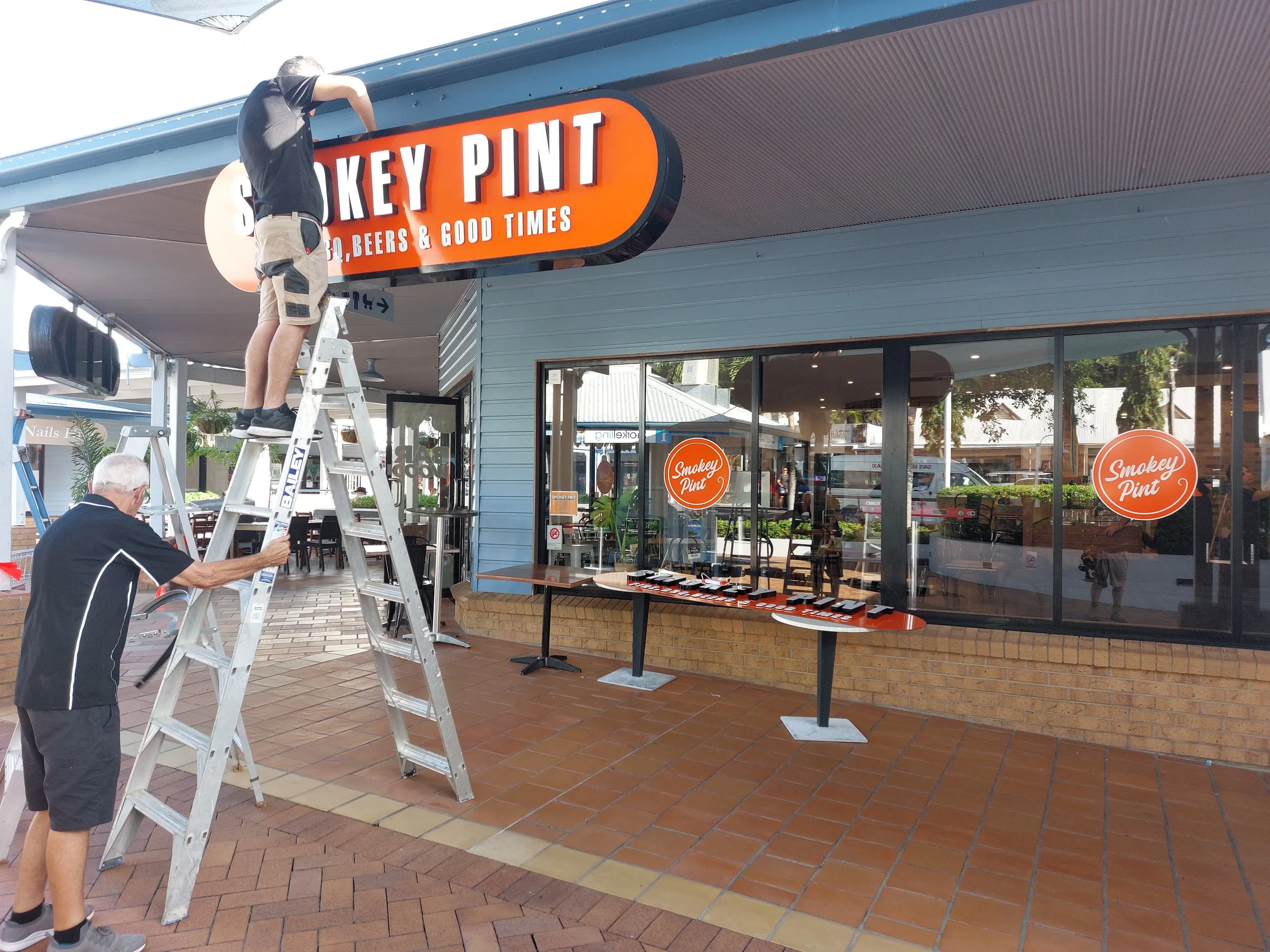 A BH Electrics electrician up an A-frame ladder working on an illuminated shopfront sign