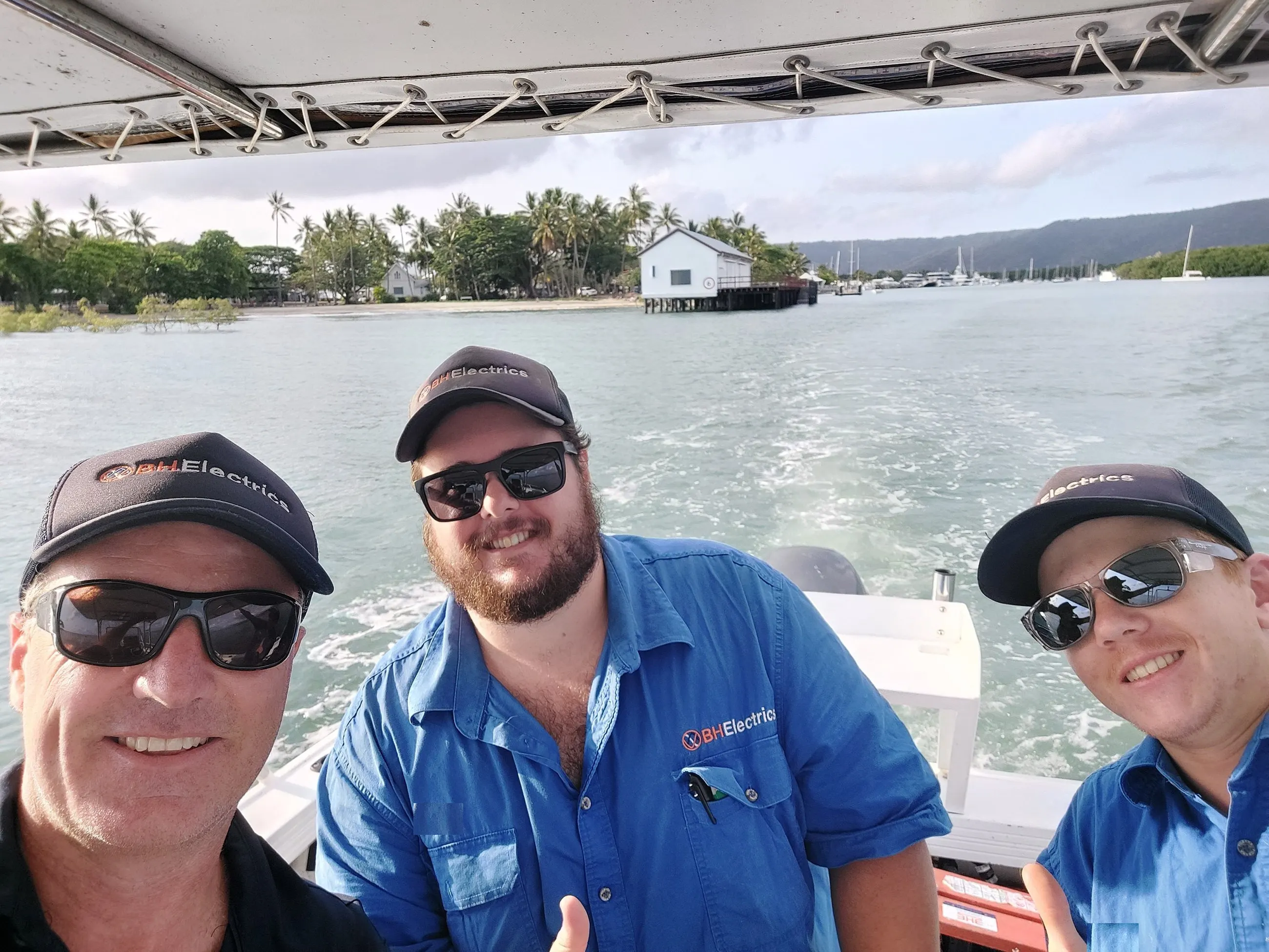 Three BH Electrics electricians in the work boat crossing the Port Douglas inlet, the Sugar Wharf and the marina behind them