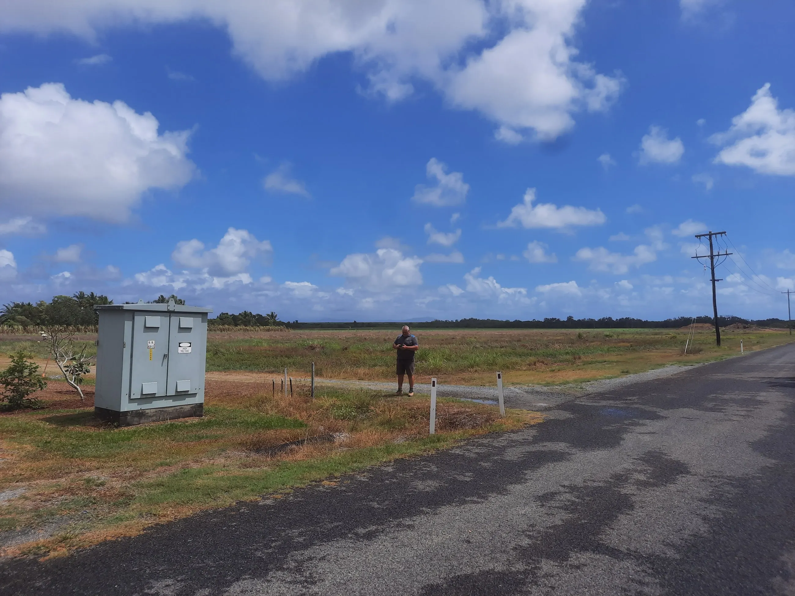 A padmount transformer kiosk beside a cane road under a big Far North Queensland sky