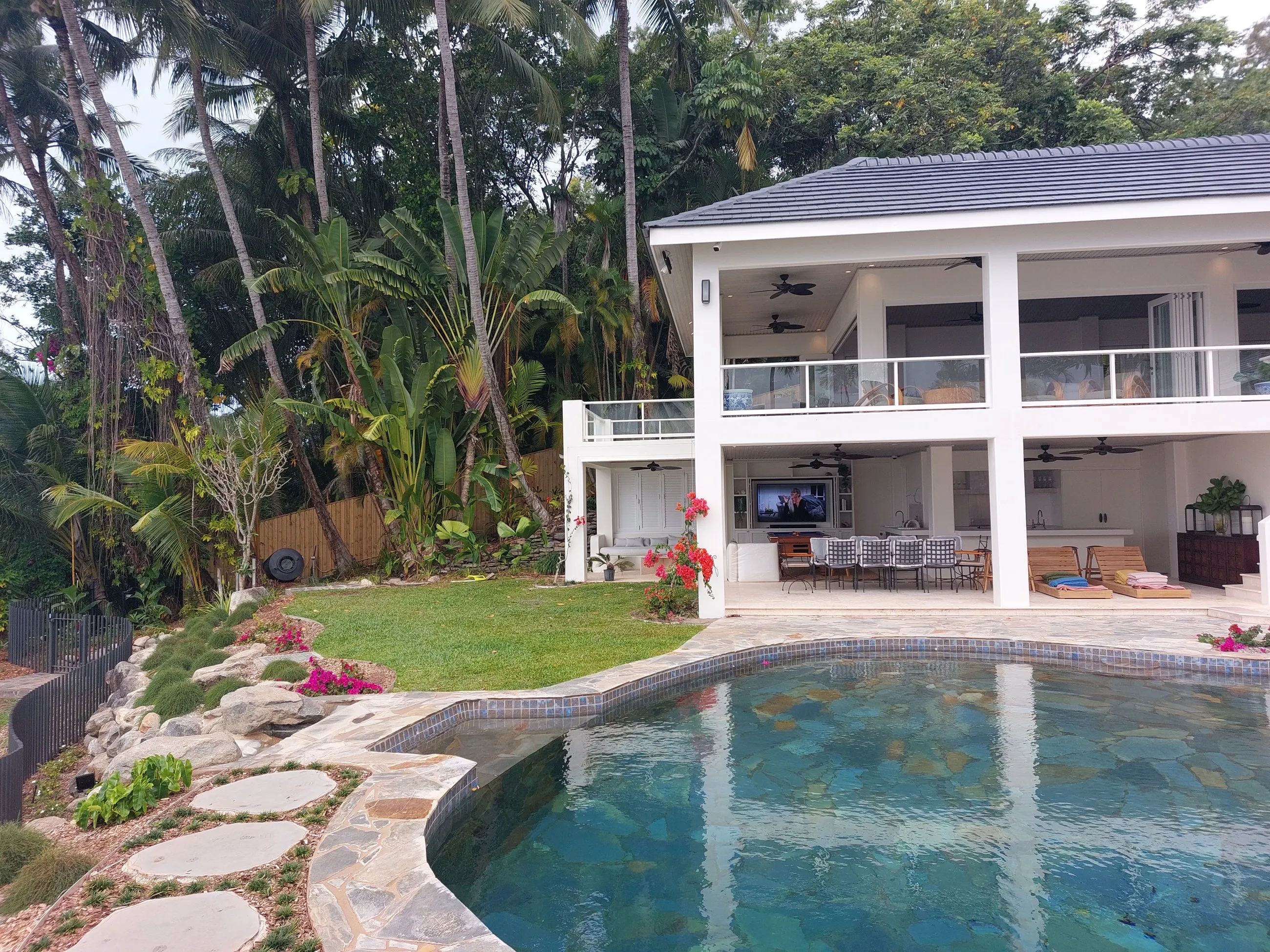 A high-set Queenslander with a pool in the foreground, palms and tropical garden around it