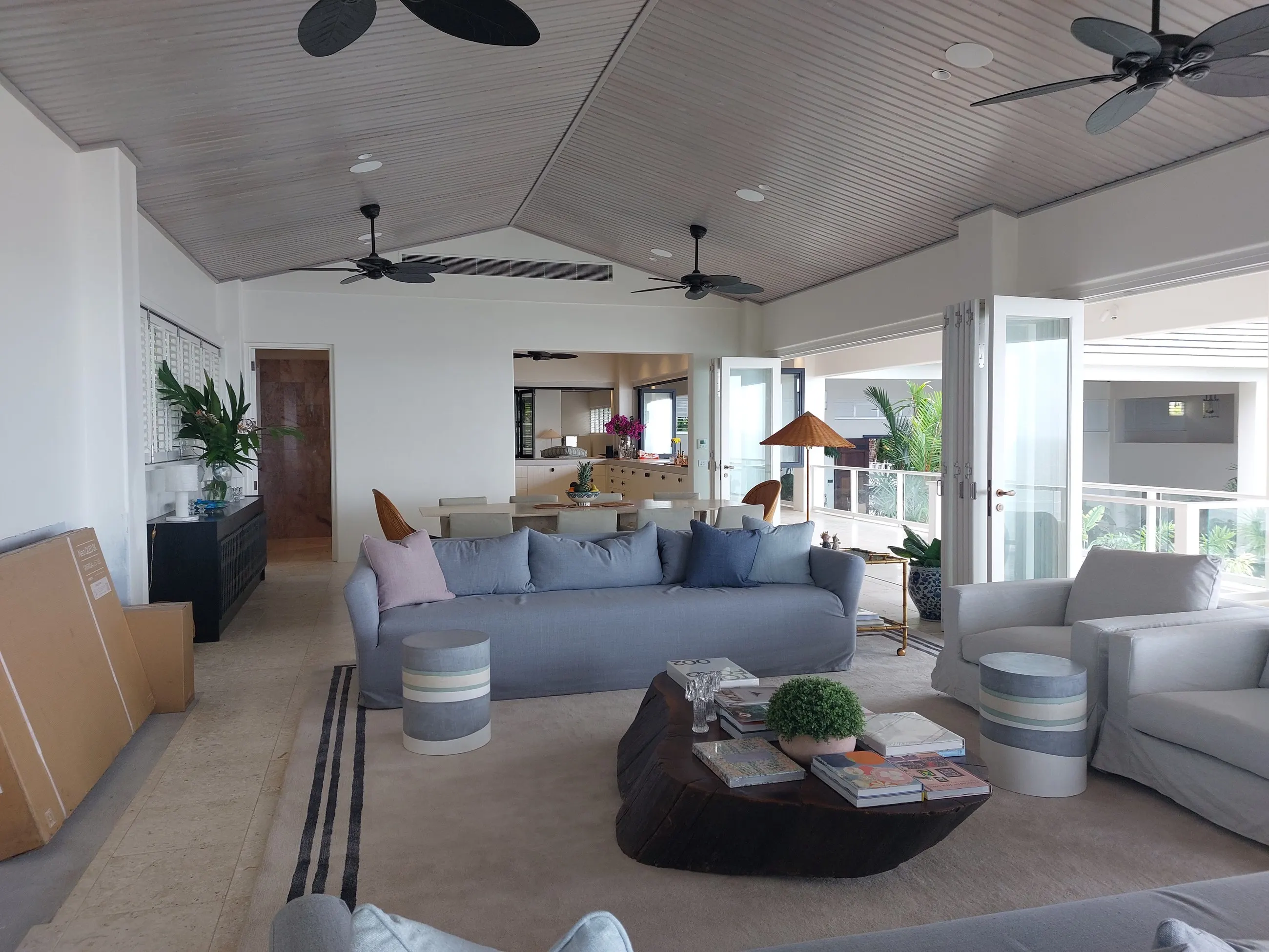 Ceiling fans running in an open plan living room with a raked ceiling, kitchen beyond