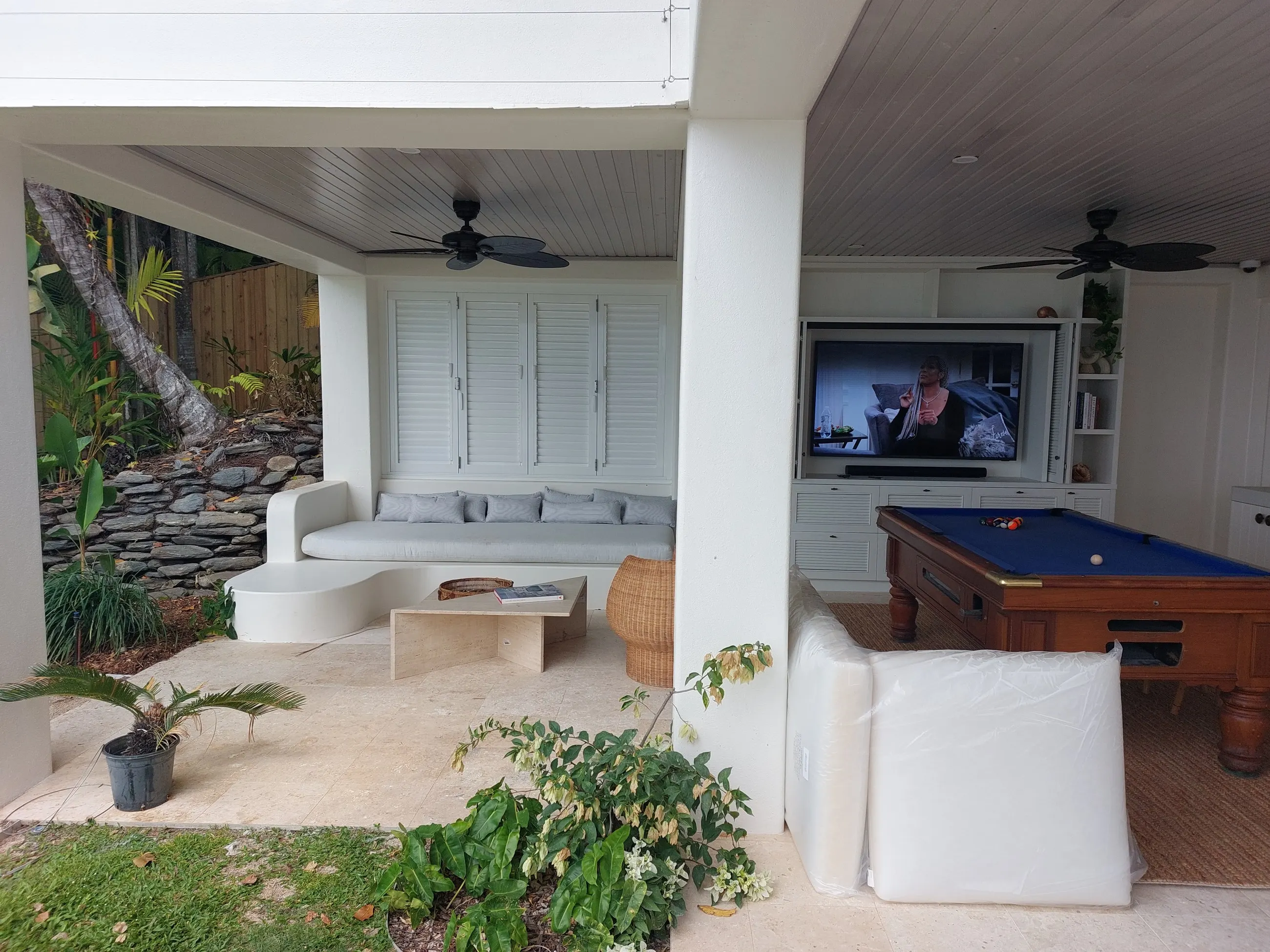 An outdoor lounge with a wall-mounted television, pool table and ceiling fan