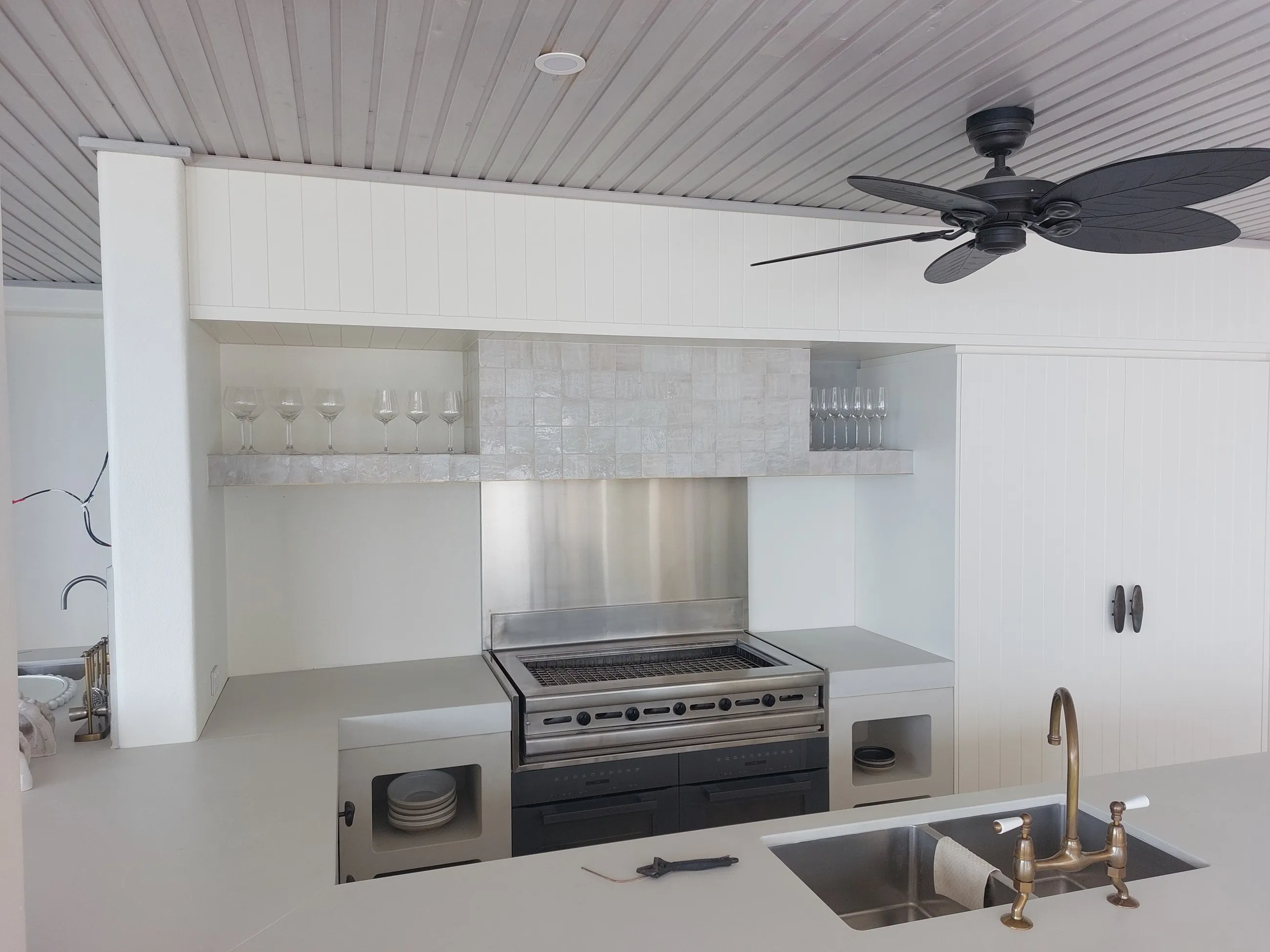 An outdoor kitchen with a built-in grill, rangehood and sink under a lined ceiling