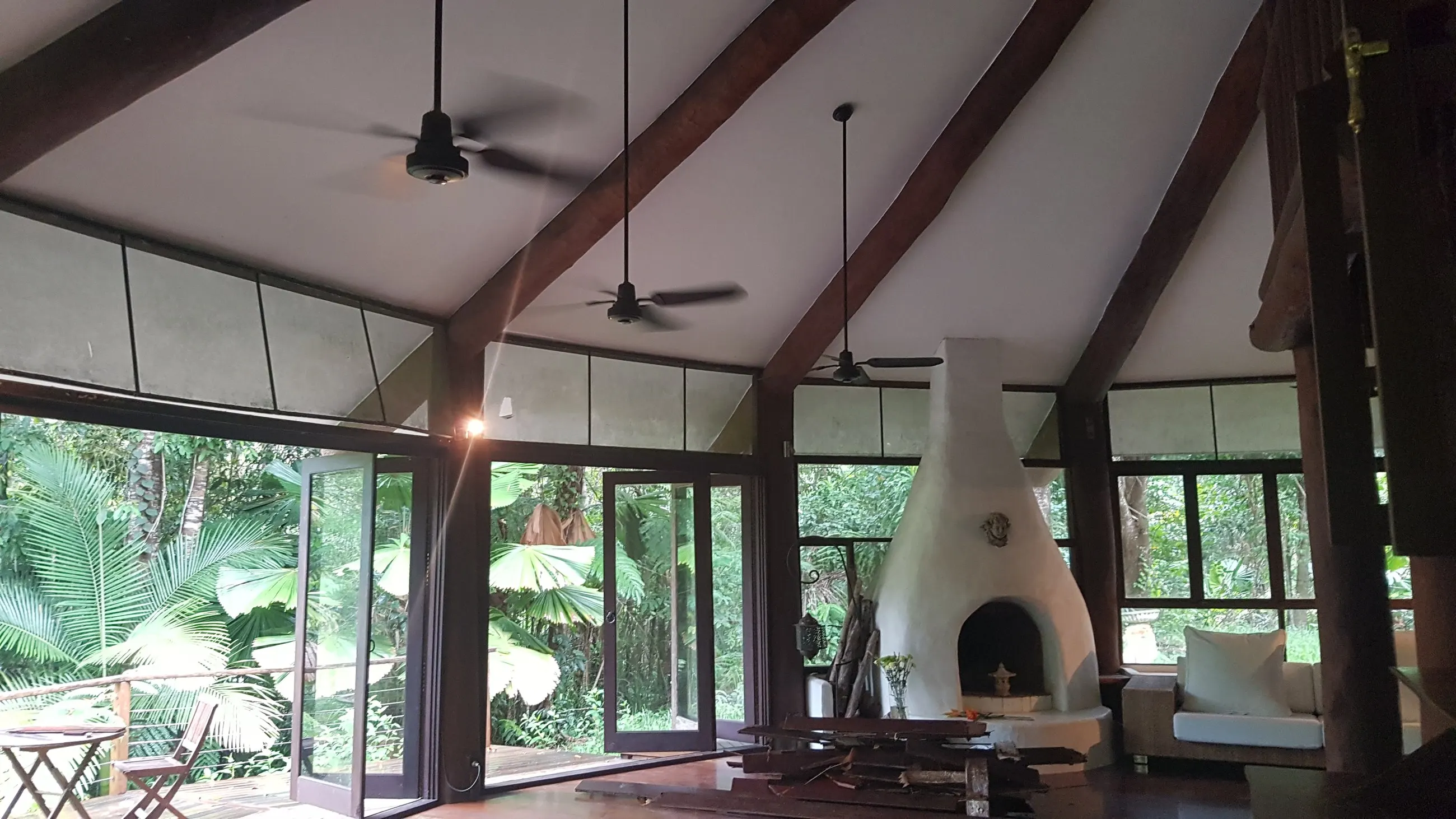 Ceiling fans on the exposed beams of a raked cathedral ceiling in a rainforest house, glass walls to the garden