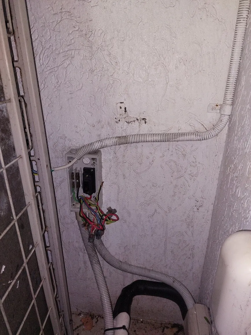 A damaged outdoor power point with corroded conduit and bare conductors hanging out of the wall