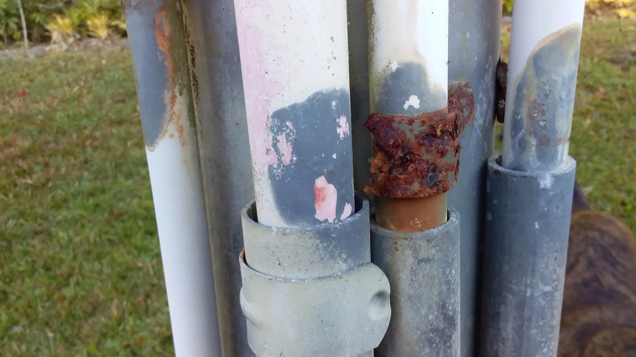 Galvanised conduit stubs eaten back by salt, rust blooming through the coating