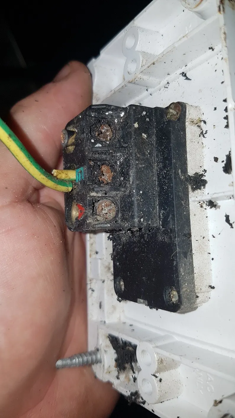 A burnt out switch mechanism in a gloved hand, the terminals charred black