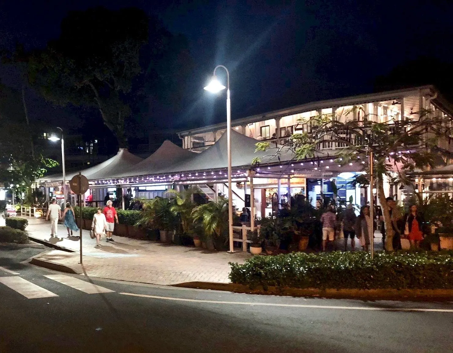 The Court House Hotel on the corner of Wharf and Macrossan Streets at night, street lights along the footpath and the marquee sails lit with festoon lights