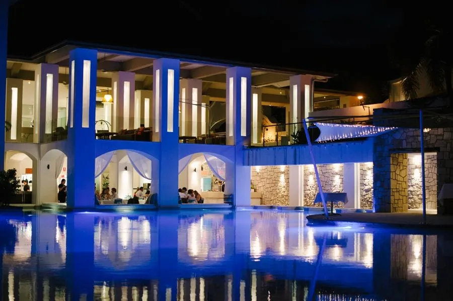 Peppers Beach Club, Port Douglas, at night, the white columns uplit blue and reflected in the pool, diners under the arches