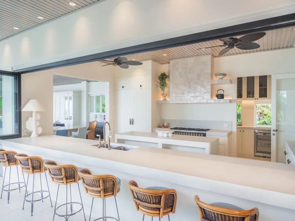The kitchen at Cliffside, downlights in the lined ceiling, palm-leaf ceiling fans, shelf lighting under the tiled rangehood and a long stone bench