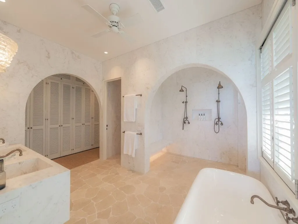 The main bathroom at Cliffside, marble walls and arches, downlights, a ceiling fan and a lit bench seat in the double shower