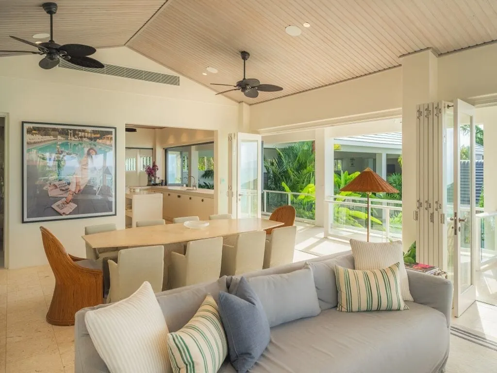 Living and dining at Cliffside, palm-leaf ceiling fans and downlights in a raked timber ceiling, bifolds open to the garden