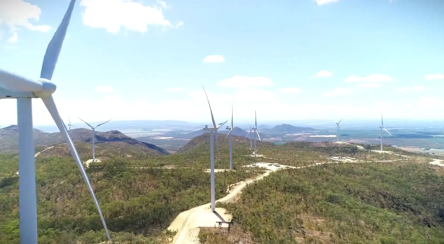 A line of wind turbines across the scrub-covered hills at Mount Emerald, access tracks winding between them