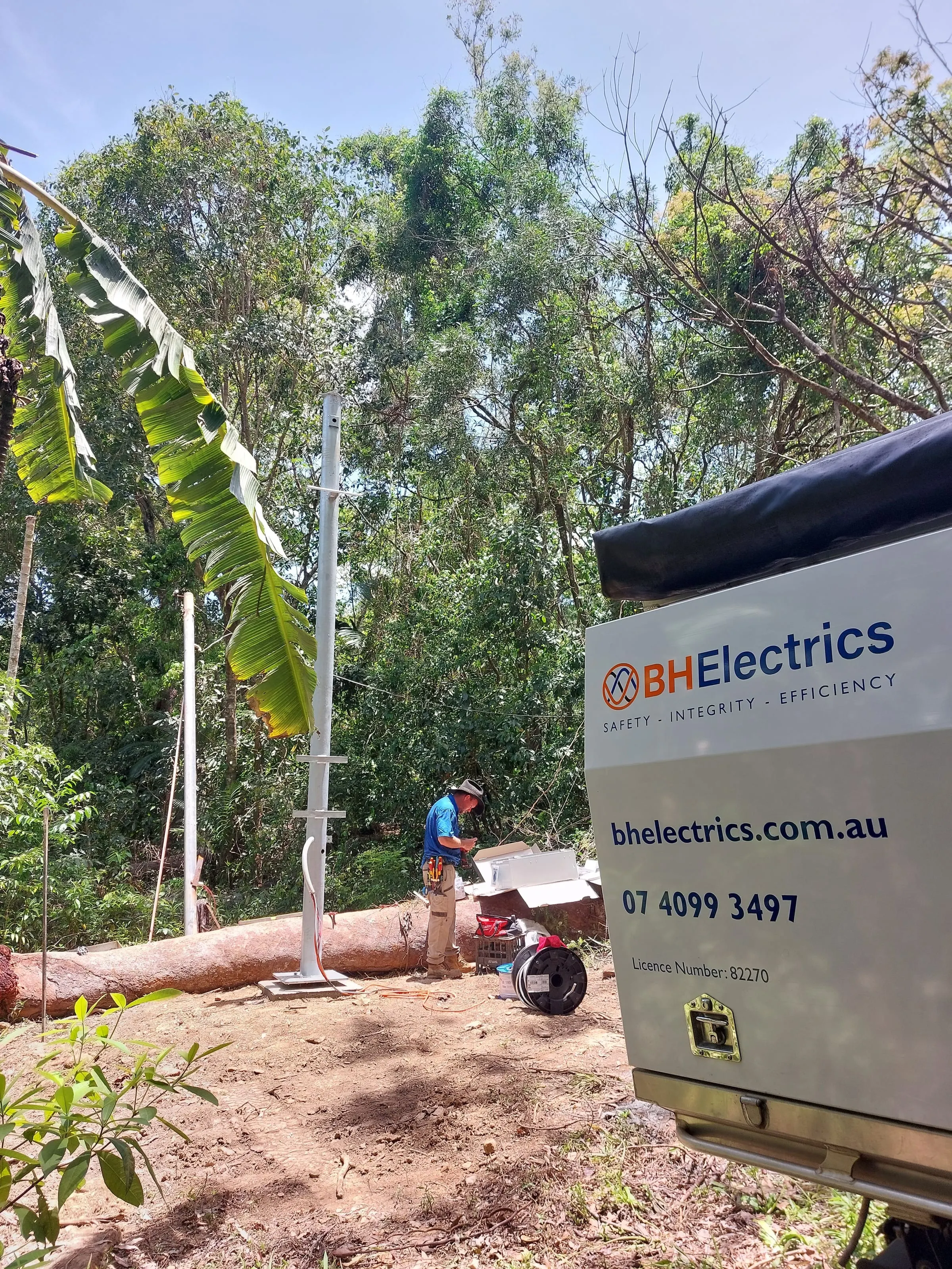 The new galvanised property pole standing on its base plate at Mowbray, an electrician unpacking the meter box beside the fallen tree