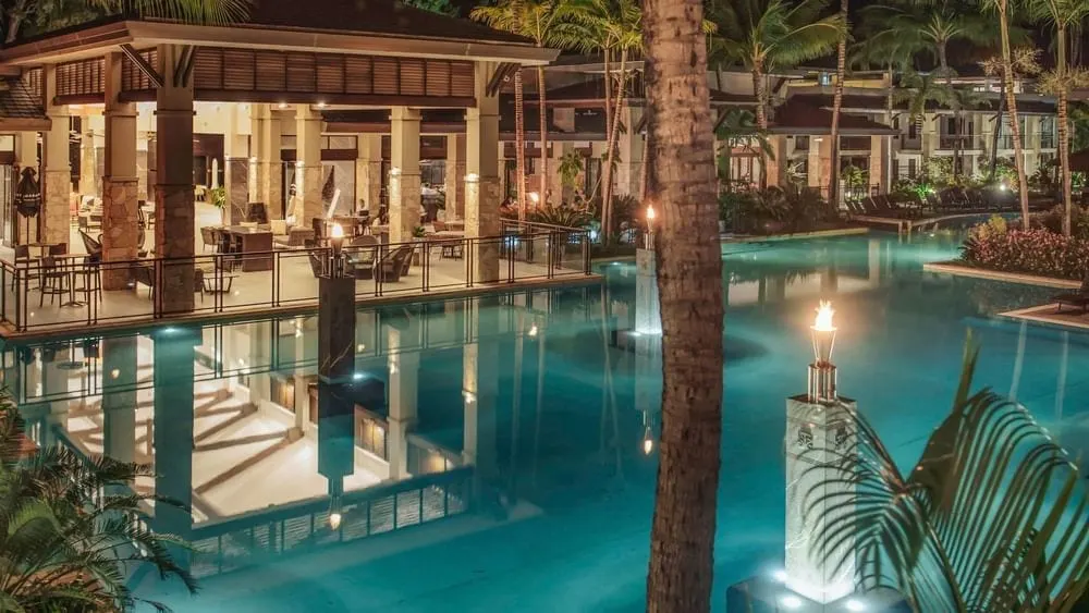Pullman Sea Temple, Port Douglas, at night: the lagoon pool lit blue, torches burning and the restaurant pavilion behind