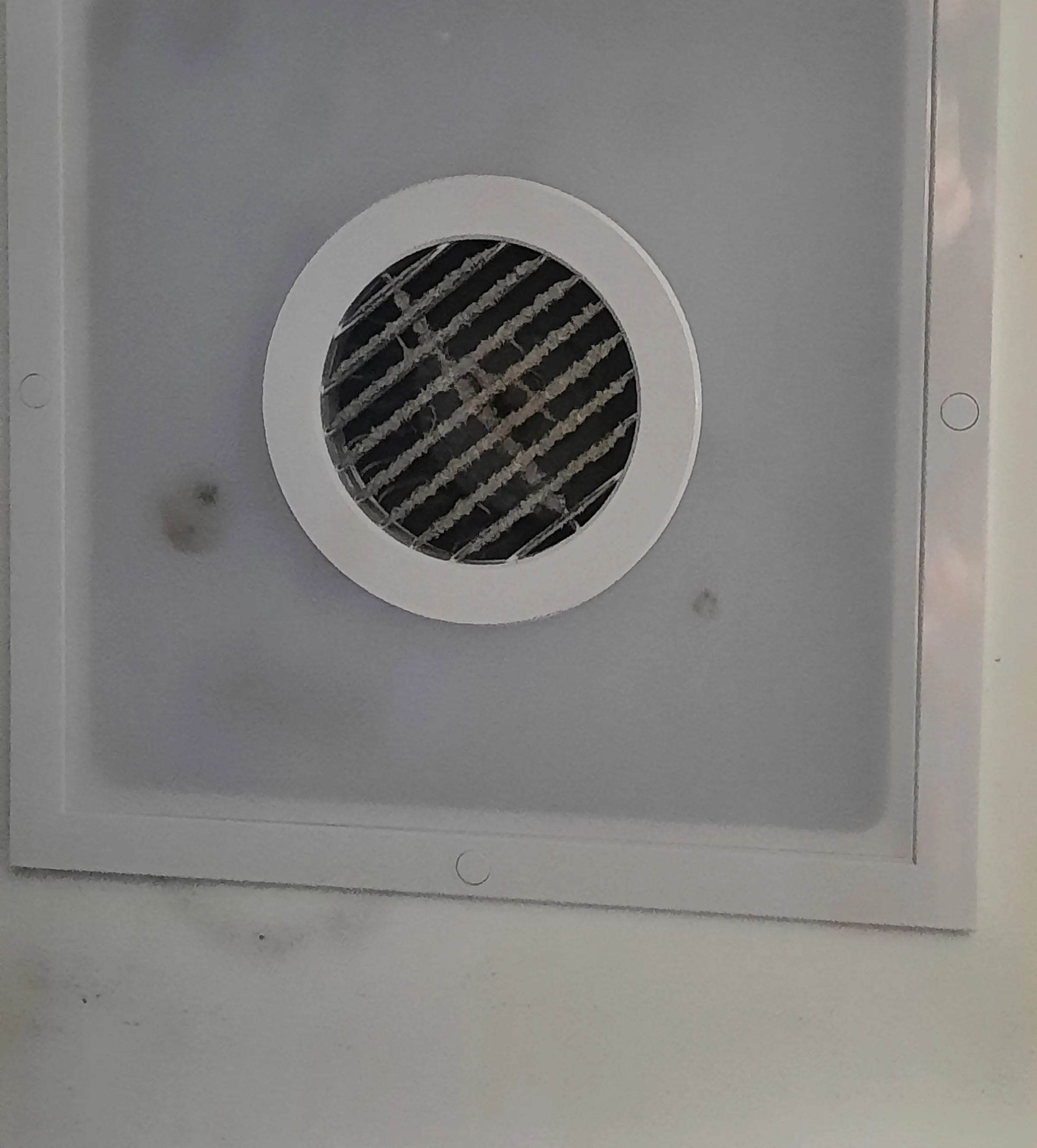 A bathroom exhaust fan grille clogged with dust, mould spotting the ceiling around it, ready for replacement